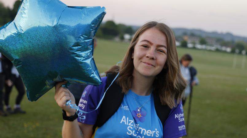 Woman smiling in a field holding a blue balloon.