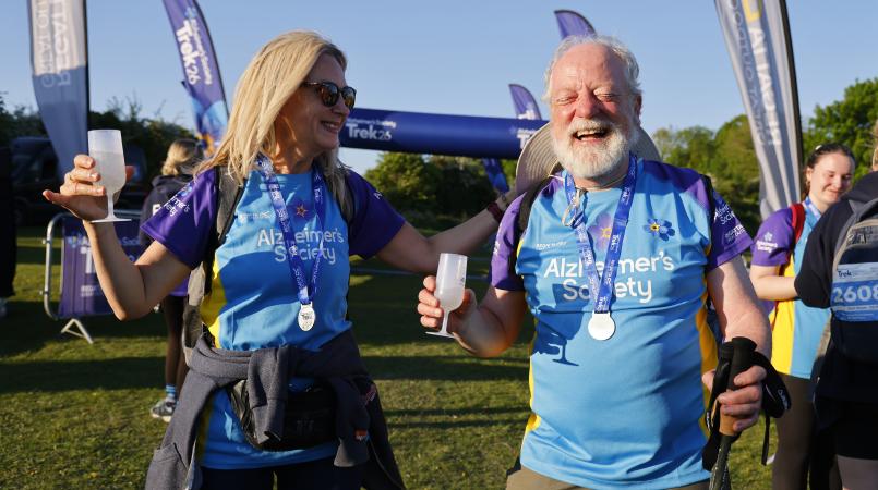 A man and woman celebrating finishing an event with their medal and glass of prosecco.