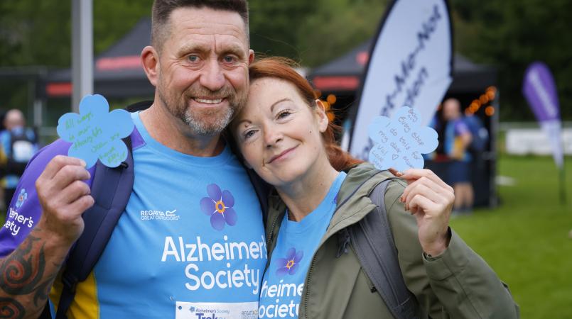 Two people smiling with a forget me not flower and a message to a loved one.