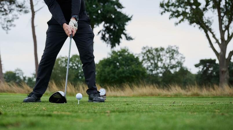 The lower half of someone's body holding a golf club next to a golf ball on a golf course