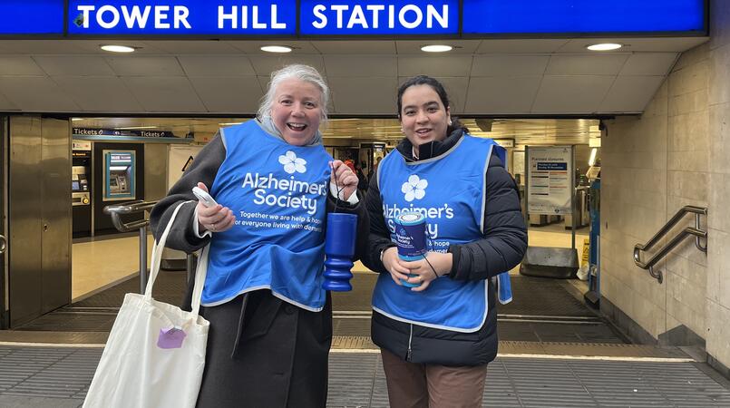 Two women in Alzheimer's Society vests smiling outside Tower Hill Station