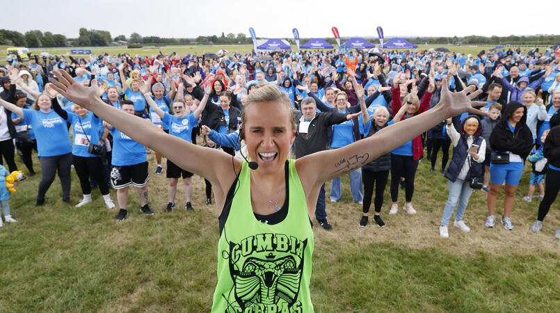 A Zumba instructor poses smiling with their arms out and a crowd of Memory Walkers behind them