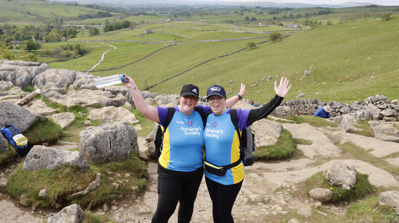 2 women with their hands in the air walking up a rocky hill