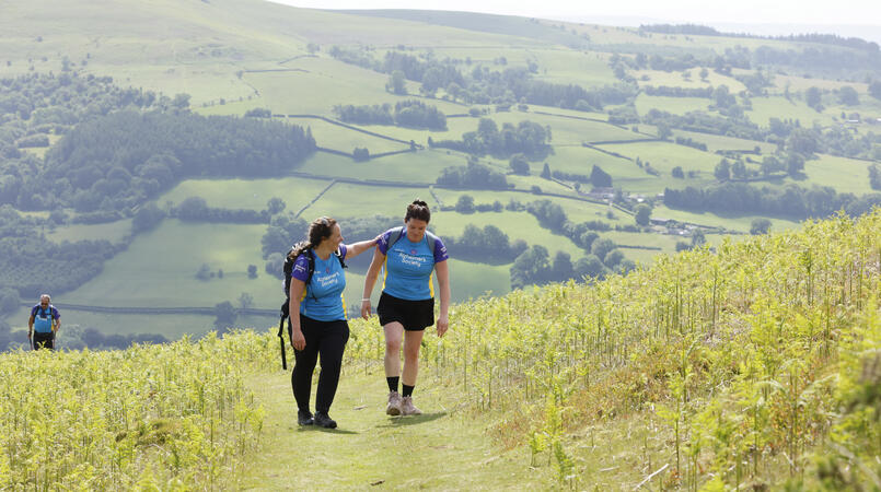 2 people wearing Alzheimer's Society tops walking towards the camera up a grassy hill.