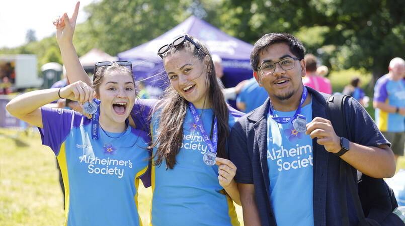 A group of 3 smiling at the camera and holding their trek26 medals