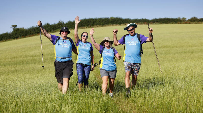 A group of four smiling in a field as they walk towards the camera.