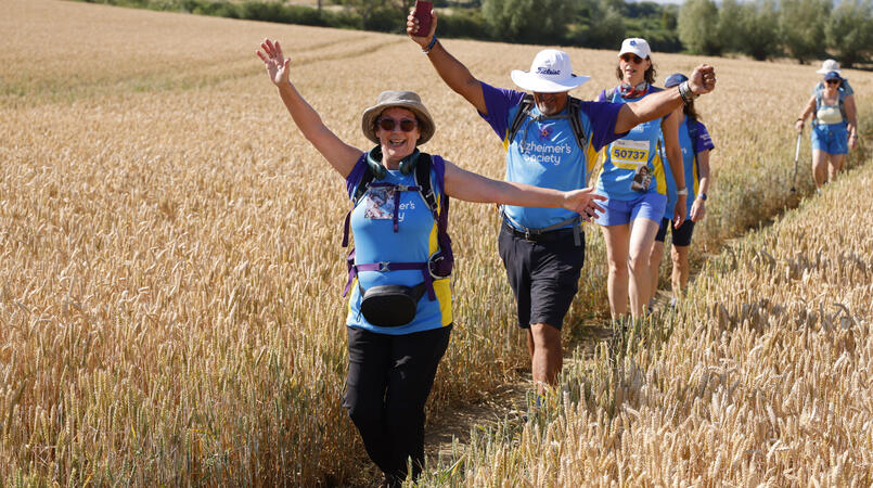 People smiling with their arms in the air as they walk through a field.