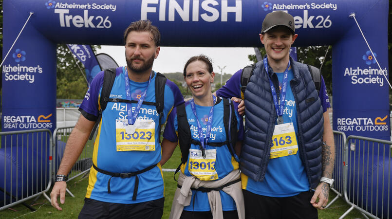 A group of 3 people smiling at a trek26 finish line.
