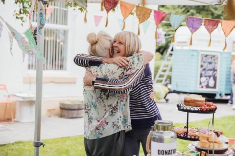 Two women hugging next to a Cupcake Day display