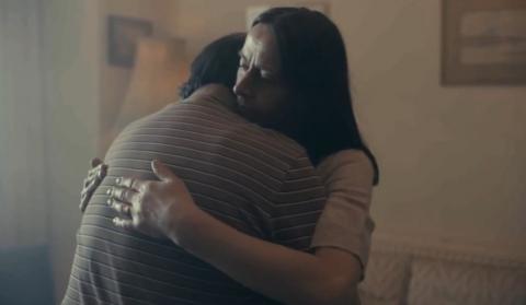 A woman is embracing a man, her husband, in their house