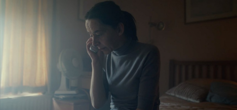 A woman is sitting in a dark room by herself talking on the phone