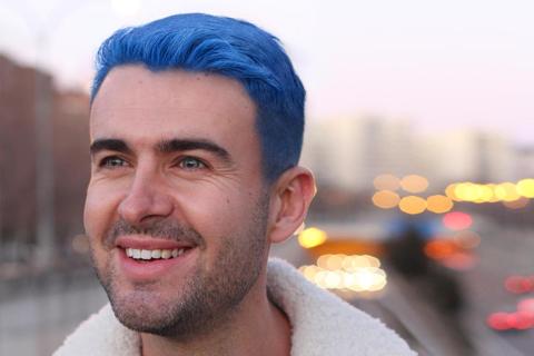 Smiling blue haired man with urban environment in the background