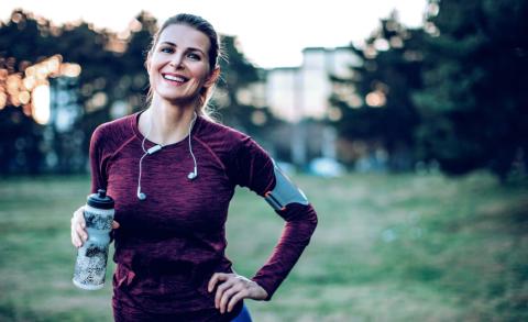 A woman smiling holding a bottle of water after just finishing a run