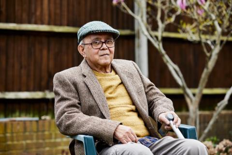 An older man sits in a chair in his garden