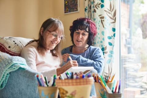 Two women sat side by side in their living room, using coloured pens to complete an activity