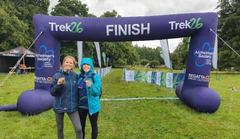 Julie and Karen under an inflatable arch that says 'Finish' at a Trek26 holding their medals
