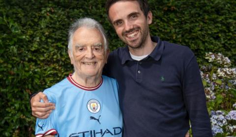 Charlie with his arm round Barry, his grandad, who is wearing a Manchester City football shirt