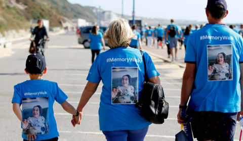 Man, woman and child, holding hands, walking away from the camera, wearing blue t-shirts with image of loved one pinned on back.