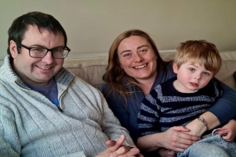 Mark and Caroline sit on the sofa with their son William