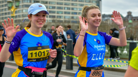 Two Alzheimer's Society runners smile and wave as they take part in race