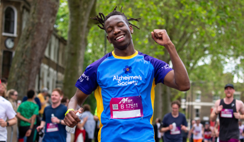 A gentleman punching the air with a mix of relief and tiredness on his face, with crowds around. He is dark skinned and wearing an Alzheimer's Society t-shirt and race number.