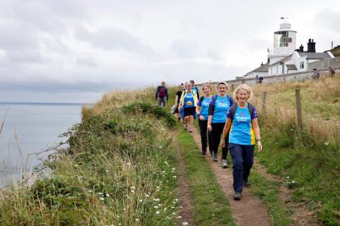 A line of trekkers on a coastal path with a lighthouse