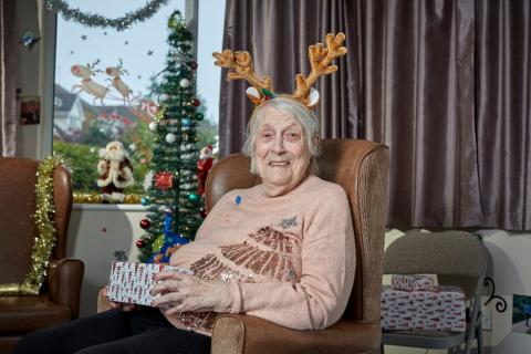 Woman sat on chair wearing reindeer ears and holding a present