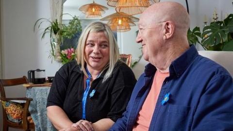 A woman with an Alzheimer's Society lanyard talks to a smiling man.