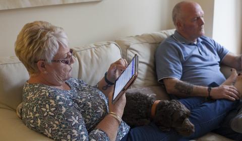 A couple sit on a sofa while using a digital tablet