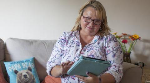 A person in a blouse is sitting on a sofa while using a digital tablet 