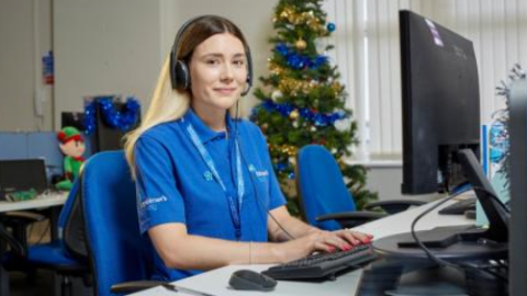 A woman in an Alzheimer's Society t-shirt sits in front of a computer in an office.