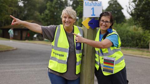Two volunteers in high vis pointing to the left and smiling