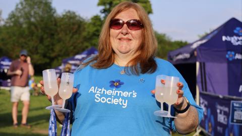 A woman with a ginger bob wearing sunglasses and an Alzheimer's Society t shirt holding medal and four glasses