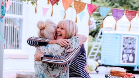 Two women embrace under party bunting