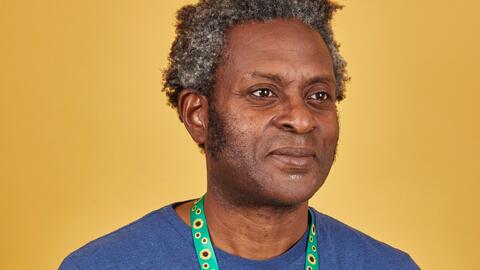 Man with grey and black curly hair wearing a blue t shirt and a sunflower lanyard