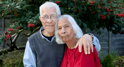 An elderly couple embrace in their garden