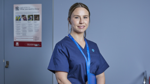 a woman in nursing scrubs stands in her practice and smiles.