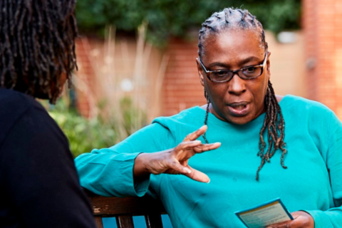 Two women talking on a bench, one holds a leaflet