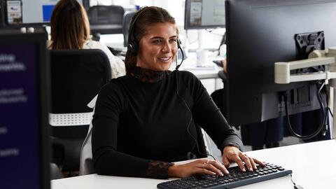 a woman in an office sitting at a desk and typing on a laptop
