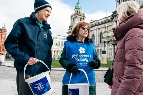 Two donation bucket collectors talking to a supporter outdoors