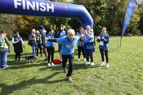 A walker in a blue Memory Walk t-shirt runs through the finish line smiling