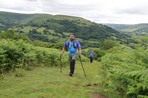 Man walking up a grassy hill with walking poles.