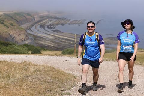 Couple walking up a coastal path with the sea in the background.