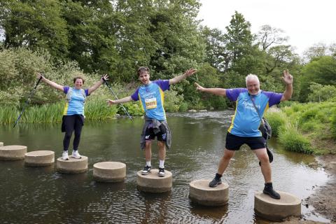 Three people crossing a river on stepping stones.
