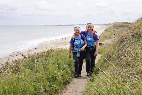 Two women smiling as they walk along a coastal path.