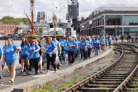 A crowd of walkers in blue Memory Walk t-shirts by the old train tracks on Bristol harbourside