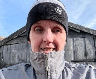 A selfie of Gill Ashington outdoors with a zipped up coat and beanie hat on