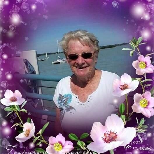 A woman with short grey hair, sunglasses and white top stood near the sea