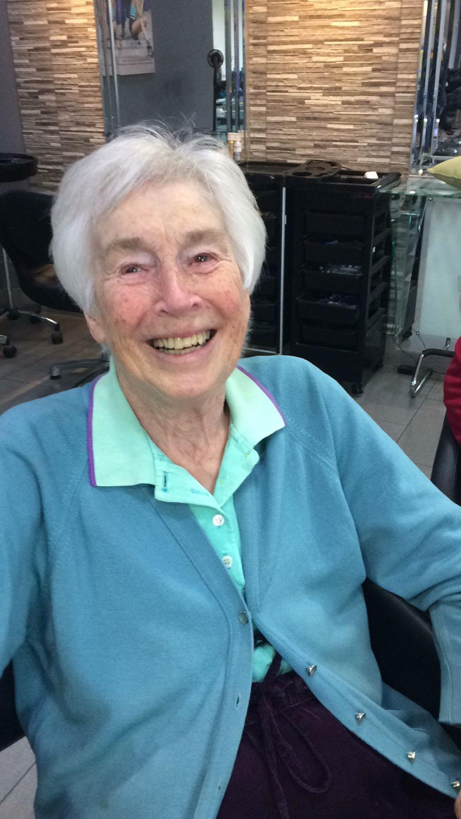 A woman with short white hair wearing a teal shirt and blue cardigan