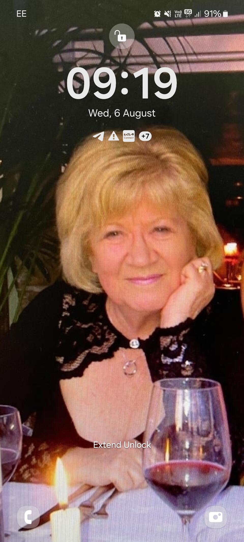 A smiling woman sat at a table with a glass of red wine